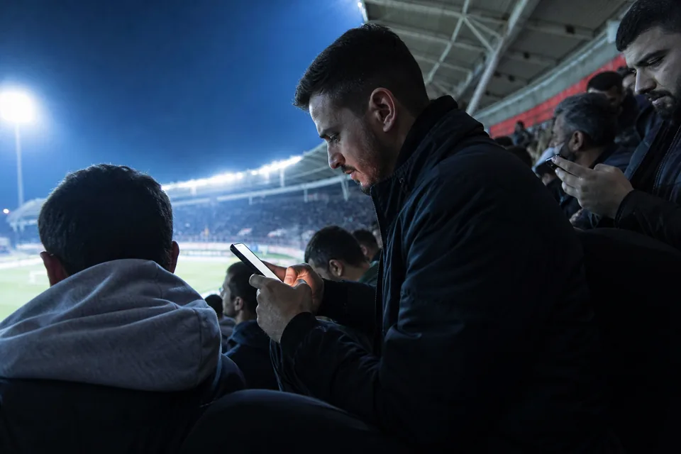 Adult fans in a stadium holding phones during a night match