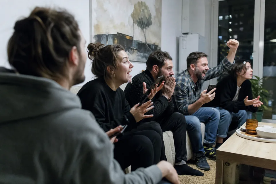 Adult friends on a sofa watching a match with phones in hand