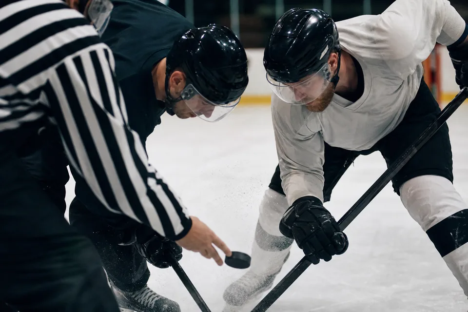 Two adult ice hockey players at a faceoff with the puck about to drop