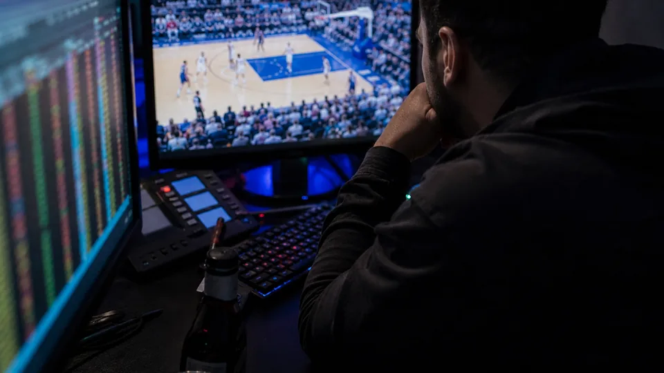 Trader watching a live basketball broadcast next to a screen of moving prices