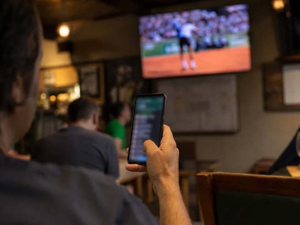 Phone in hand in a sports bar seconds before a tennis serve, the moment a next point micro-market is open