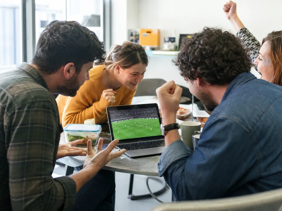 Coworkers around a laptop at lunch watching a live match together