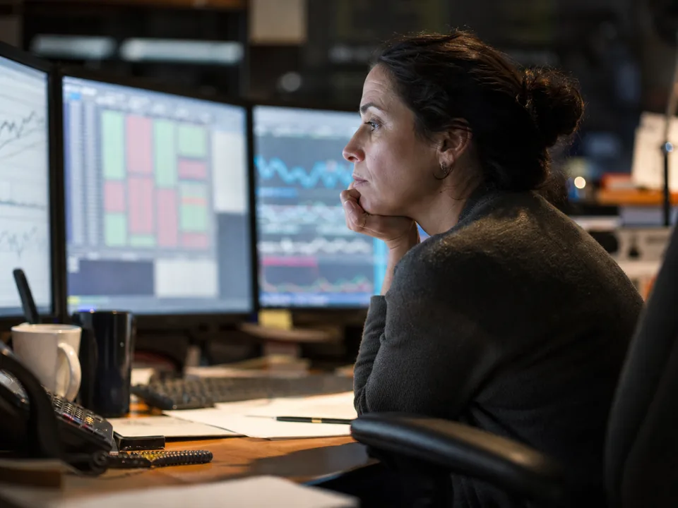 Risk analyst studying charts on three monitors at night